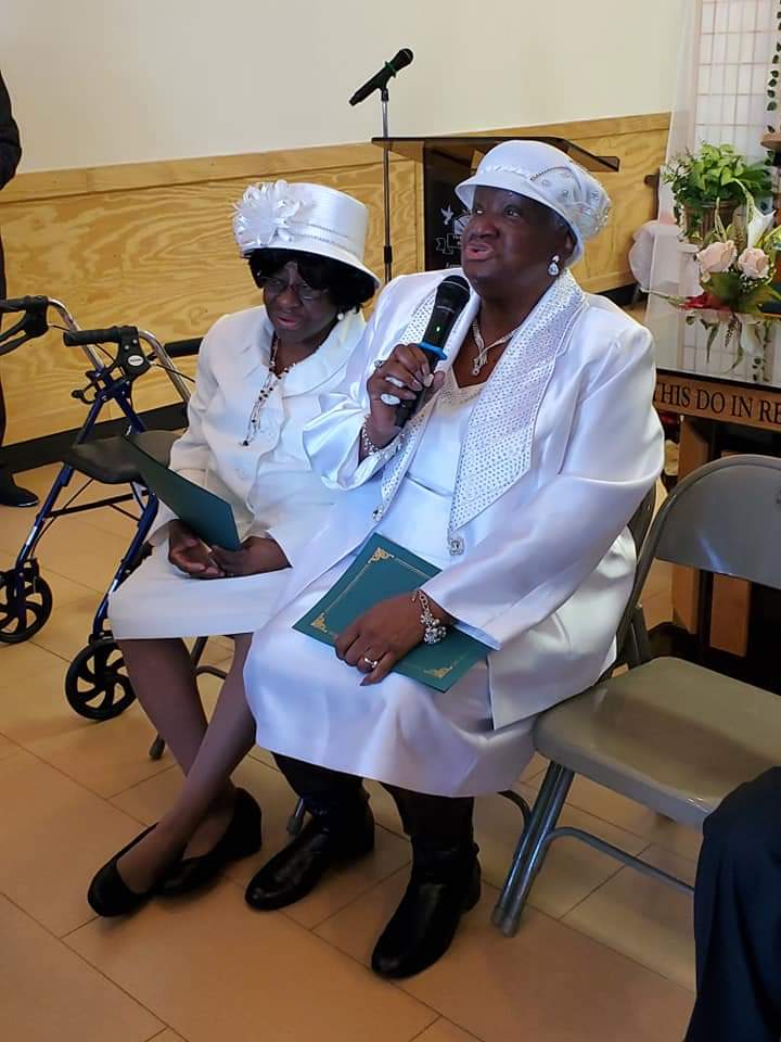two women in white dresses are sitting next to each other and one is holding a microphone .