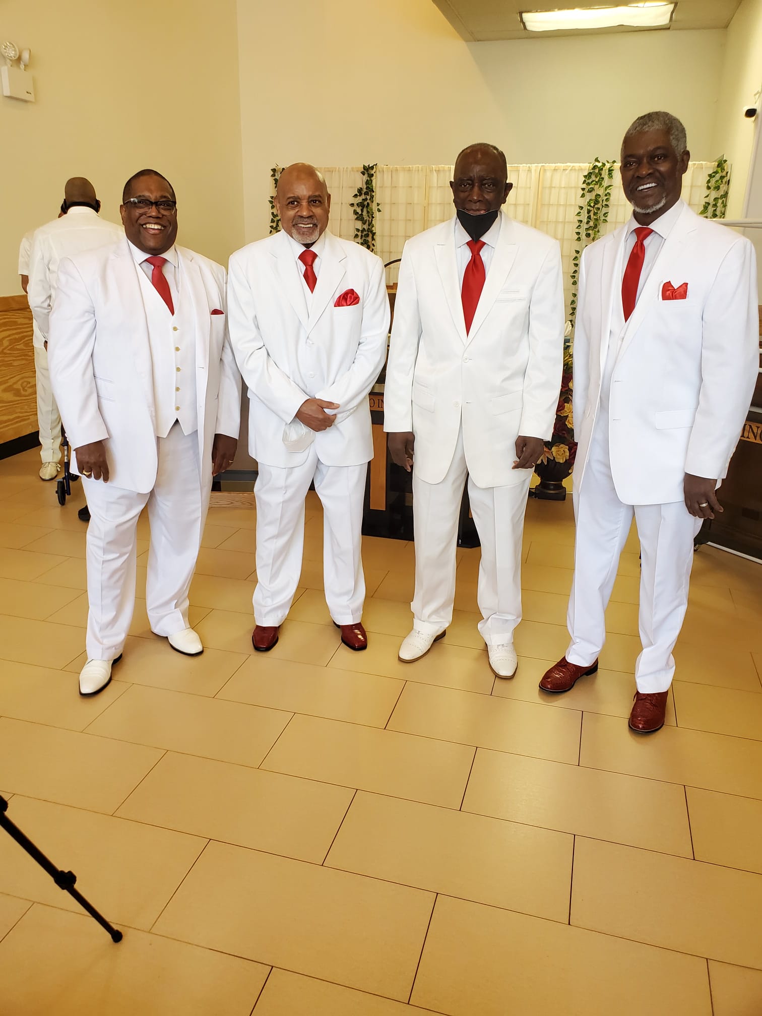a group of men in white suits and red ties are standing next to each other .