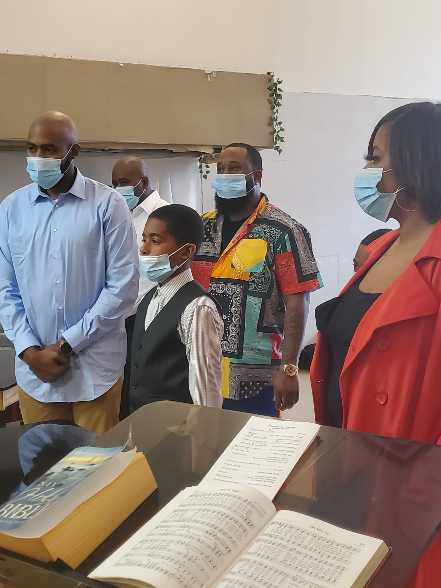 a group of people wearing face masks are standing around a table .