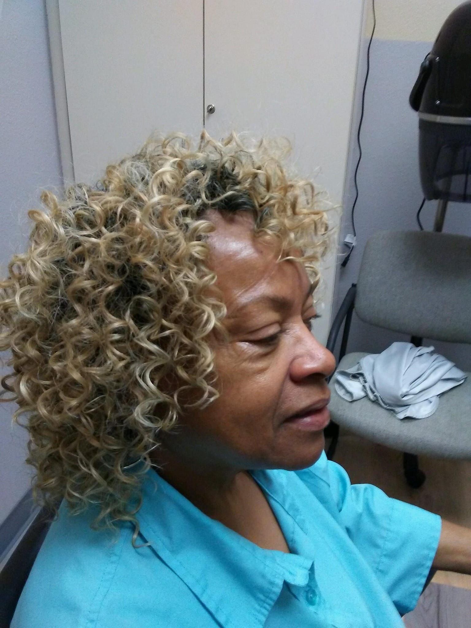 Woman with blonde, curly hair, in a light blue shirt, indoors.