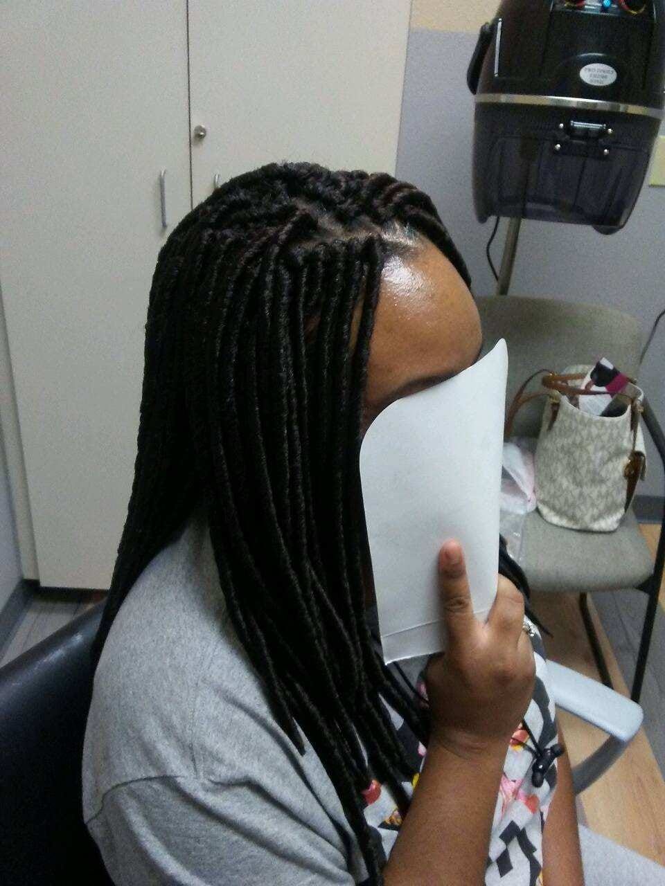 Person with long, black box braids holds white paper in front of face. Sitting in salon.