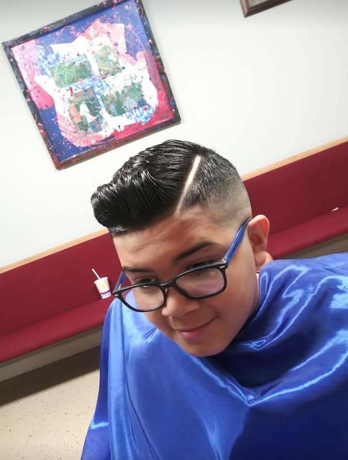 Person with glasses and a stylish haircut in a barbershop. Wearing blue cape, smiling.