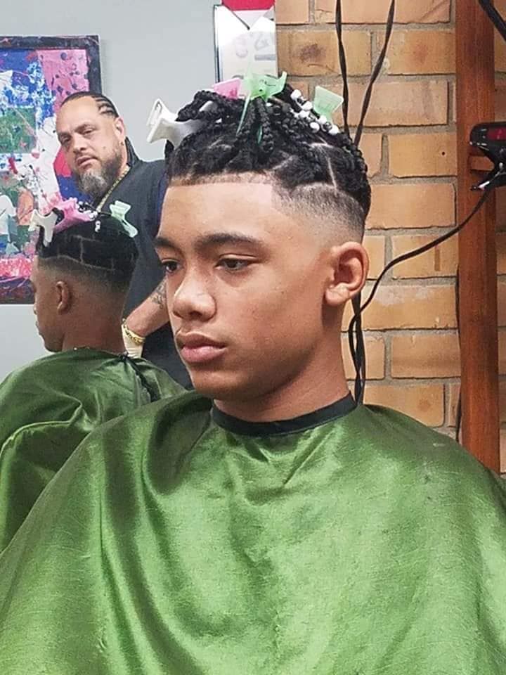 Boy with braided hair getting a haircut, barber in background.