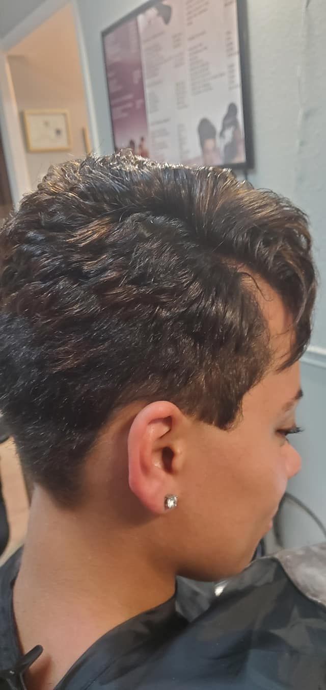 Person with short, dark, textured hair, wearing a black salon cape, in a salon setting.