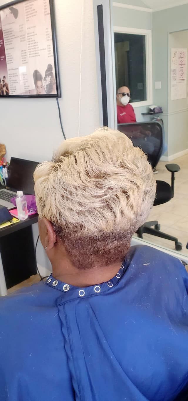 Person with blonde and brown hair in a salon chair, facing away from the camera. The stylist is in the background.