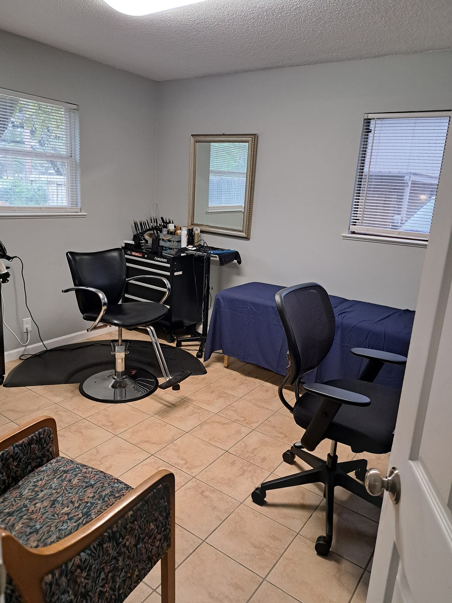Small room with salon chair, mirror, table, and two windows.