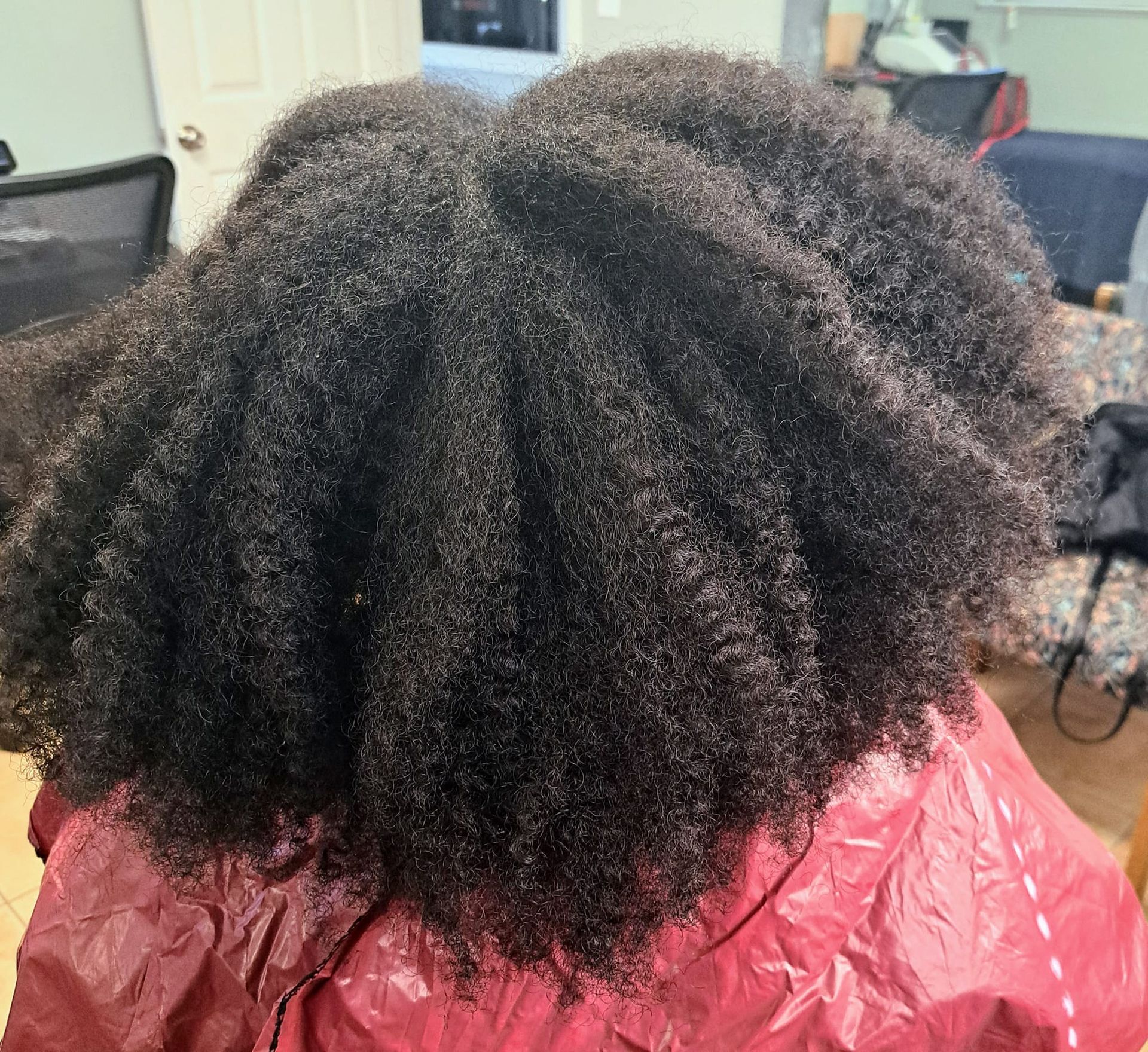 Close-up of thick, dark, textured hair on a person wearing a red cape.