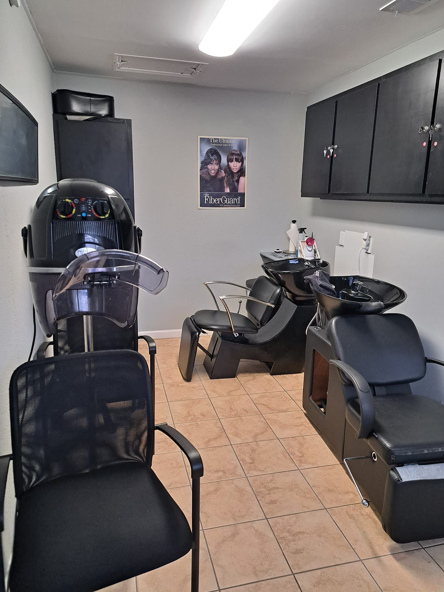 Hair salon interior with styling chairs, dryer, wash station, and storage cabinets.