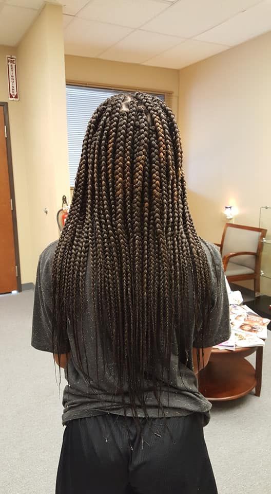 Person with long box braids, viewed from the back, wearing a gray shirt, in an office setting.