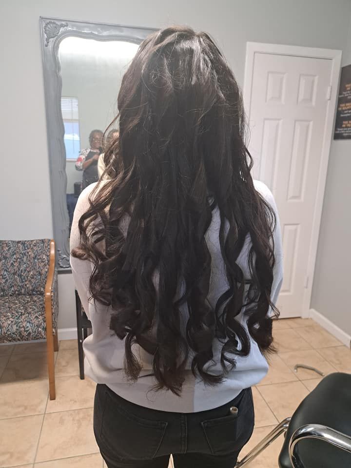 Woman with long, wavy dark hair in a salon, standing in front of a mirror.