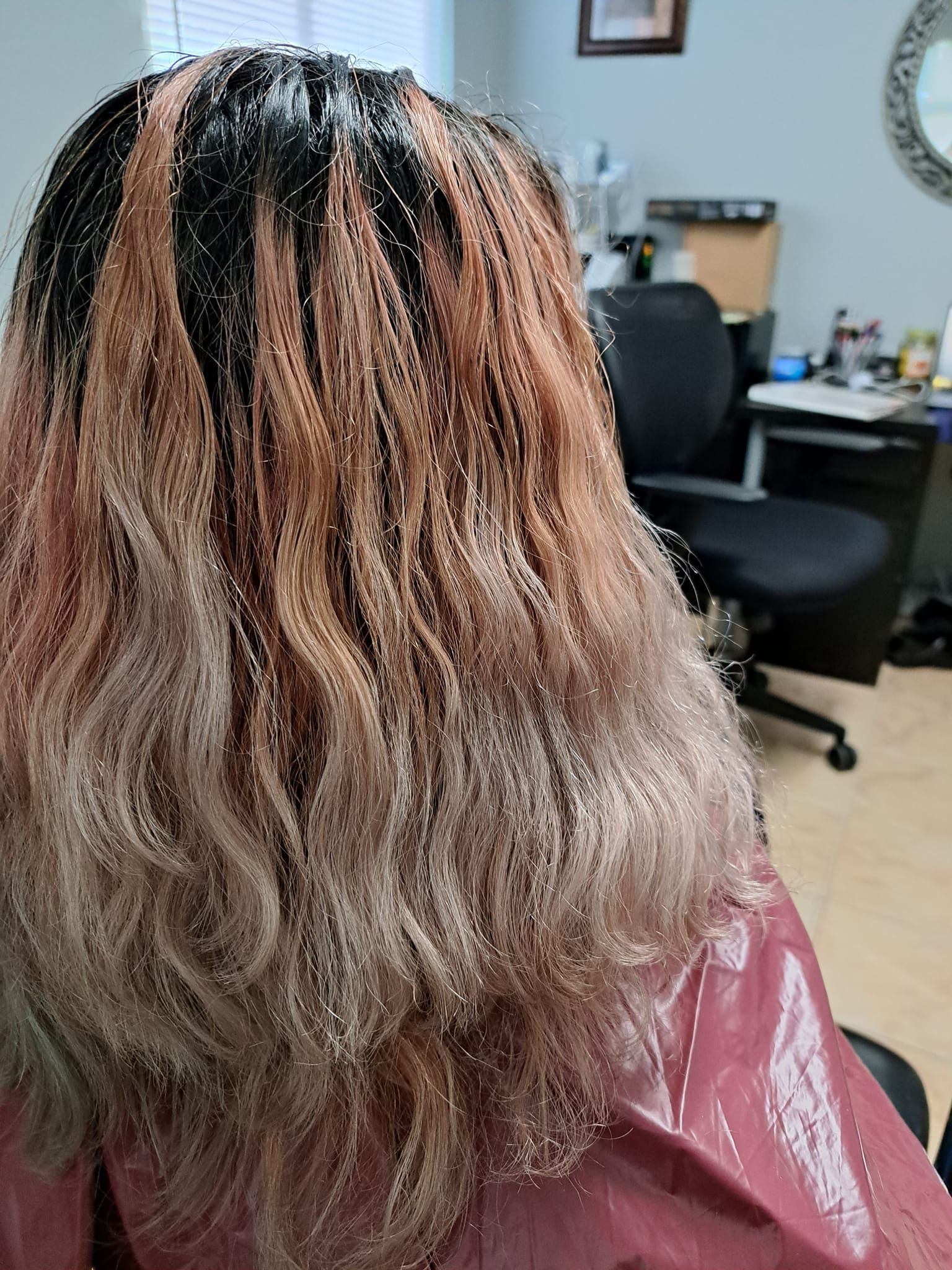 Person with hair extensions, black, light brown and blonde, in a salon setting.