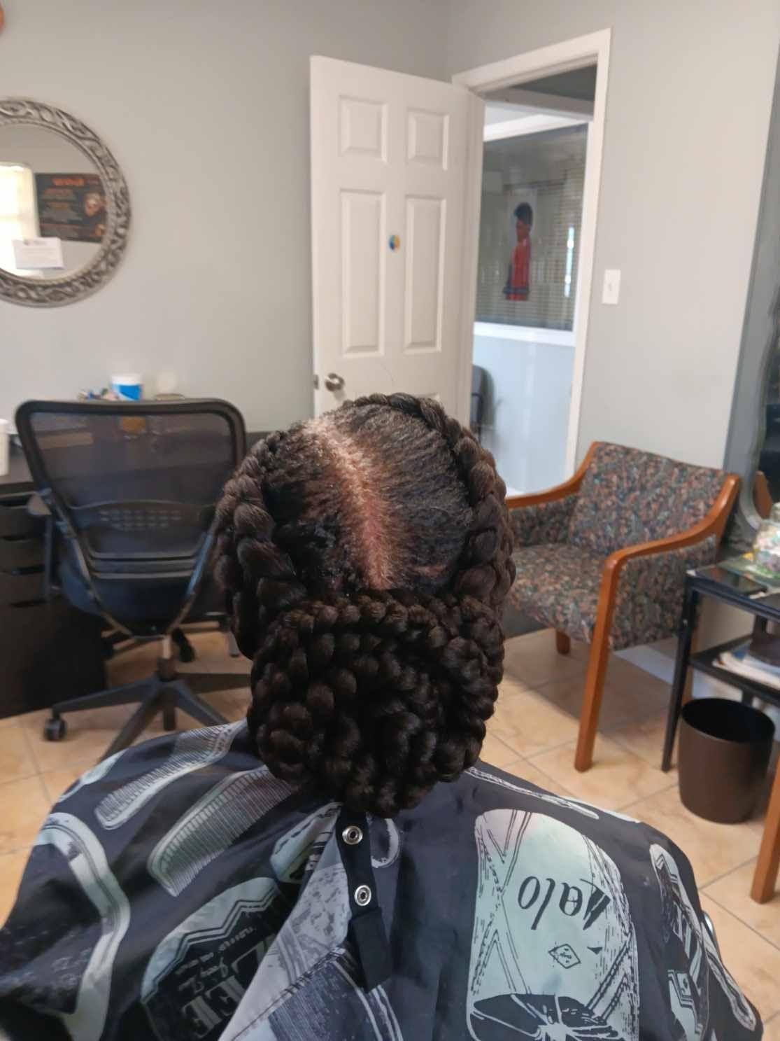 Woman with braided hairstyle, viewed from behind, in a salon. Braids are dark brown and gathered.