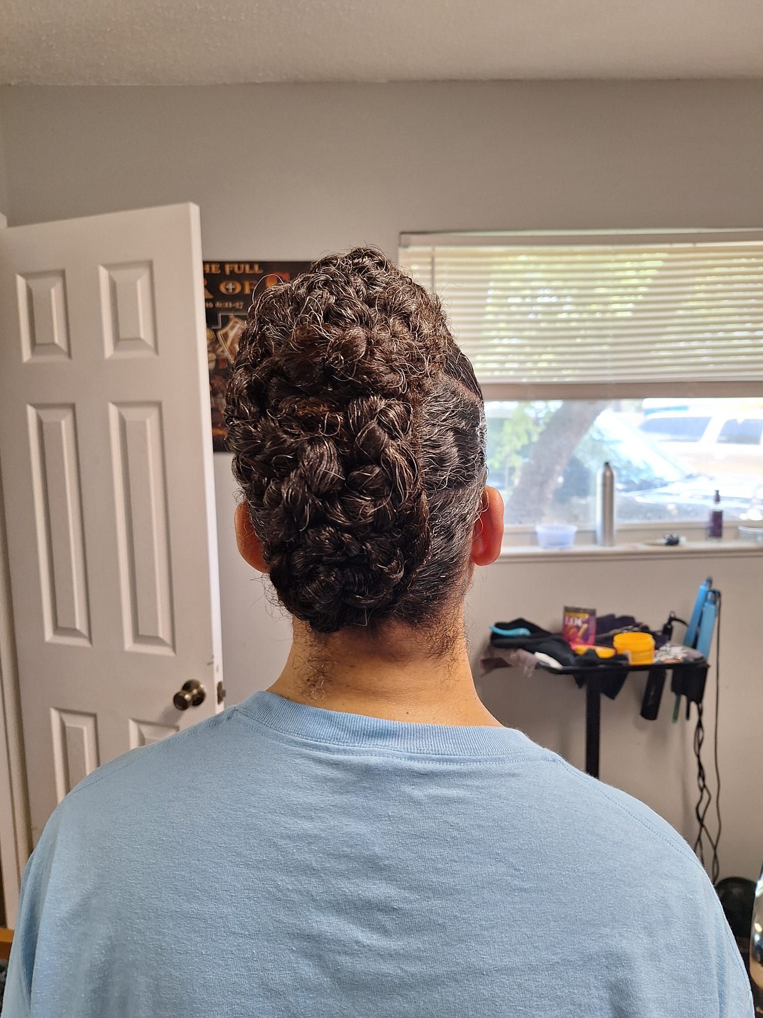 Person wearing a light blue shirt; back of head with curly dark hair; room with a closed white door and window.