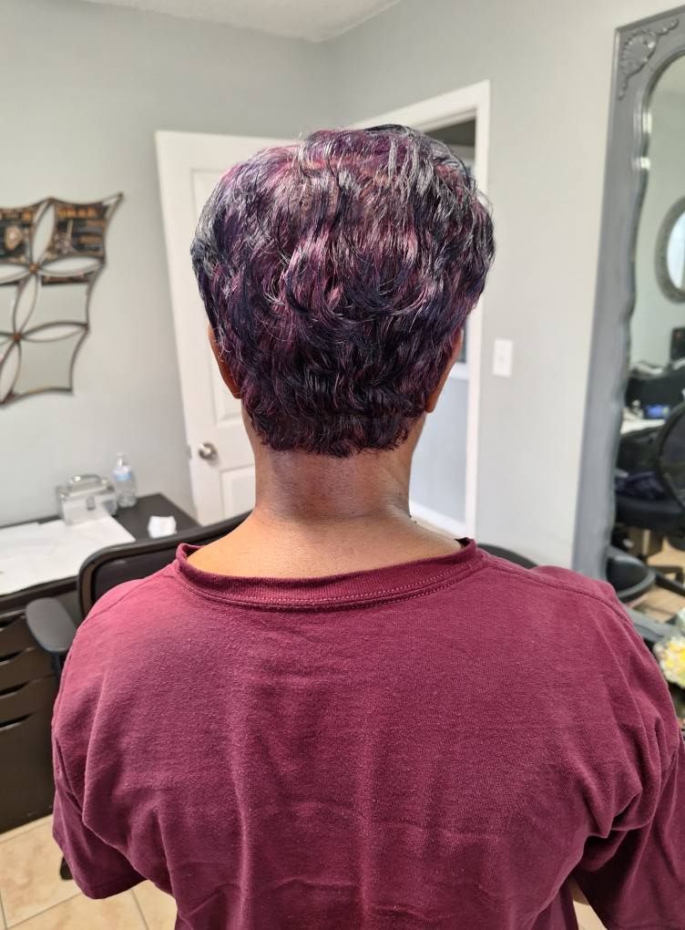 Back view of a person with short, dark purple hair, wearing a burgundy shirt, in a salon.