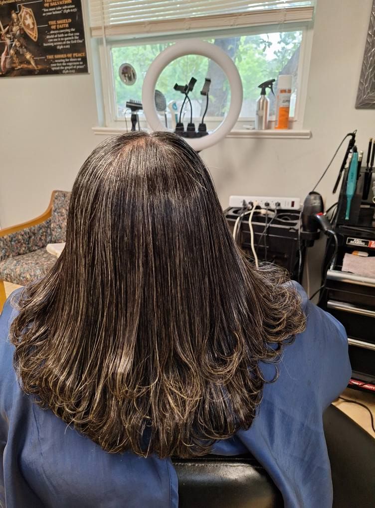 Woman with dark hair in a salon chair, back to the camera, illuminated by a ring light.