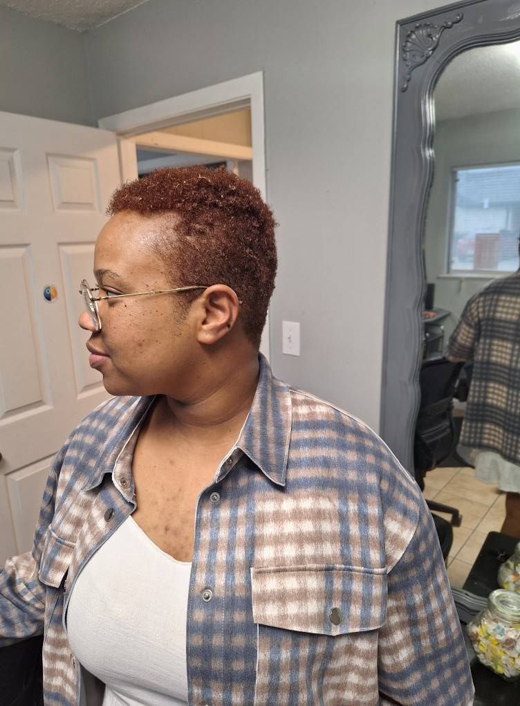 Woman with short, reddish hair and glasses in a plaid shirt. Standing in a room with a mirror and a door.