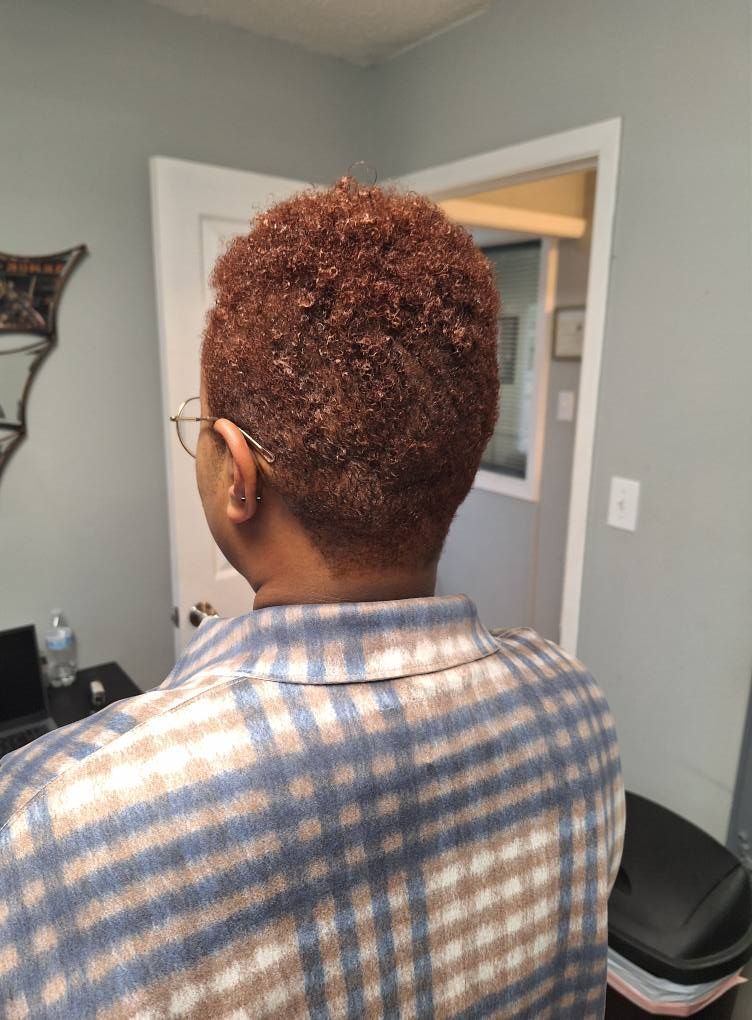 Person with short, reddish-brown curly hair, wearing glasses and a plaid shirt, standing in a room.