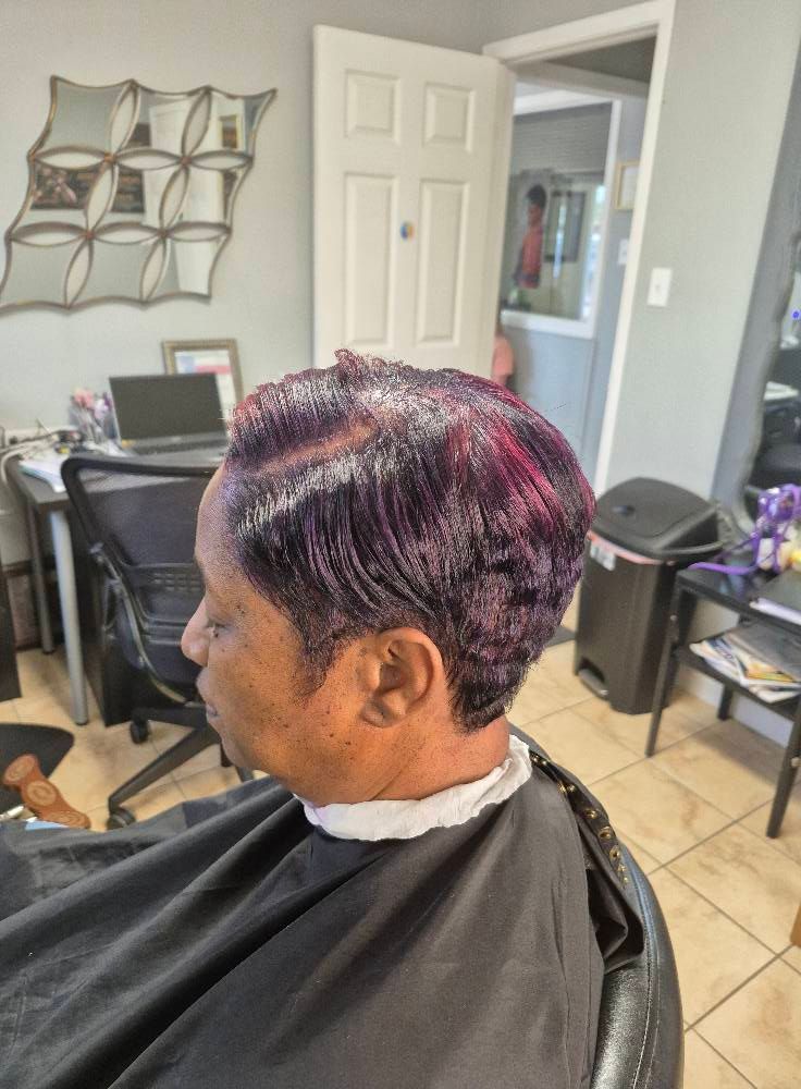 Person with a short, dark hairstyle with purple highlights, seated in a salon chair.