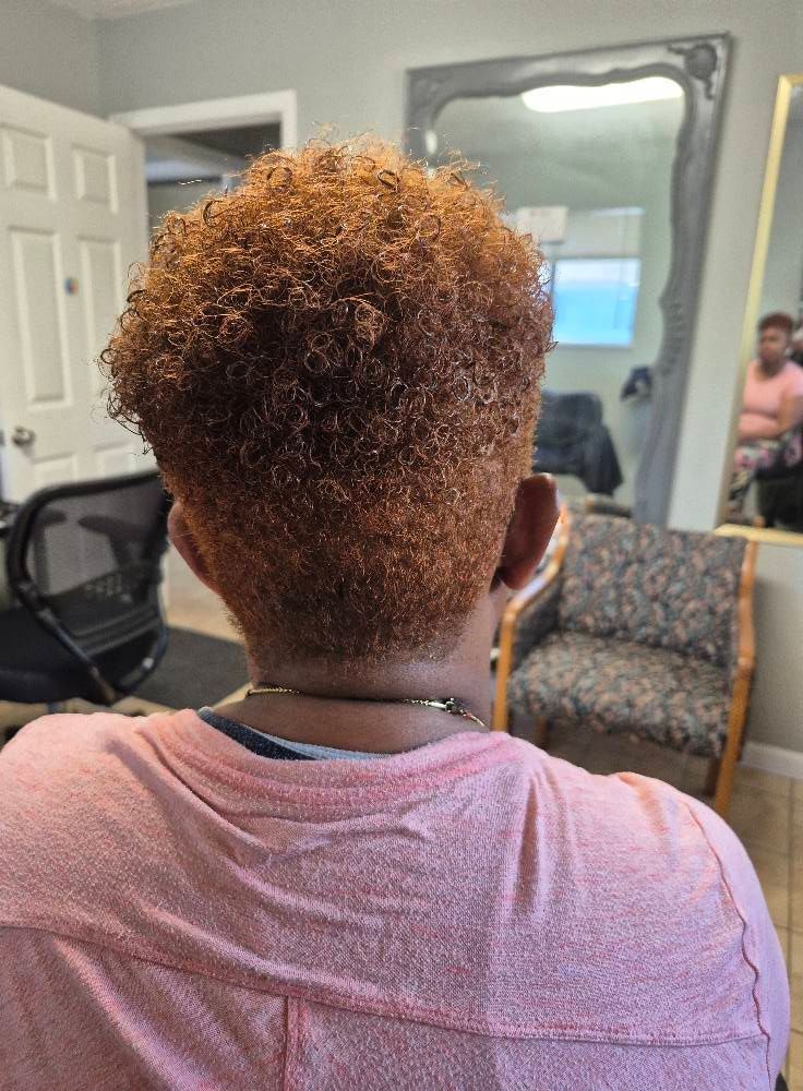 Person with reddish-brown, curly hair in a salon; they wear a pink shirt.