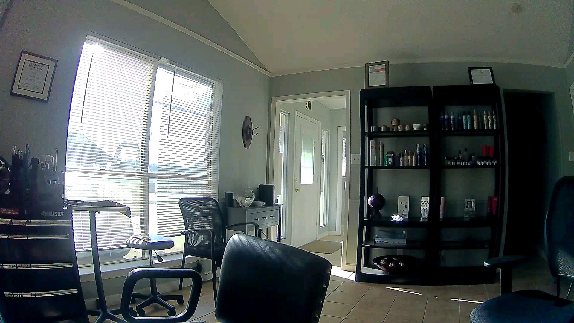 Interior of a room with a large window, shelves, and chairs. Sunlight streams through the window.