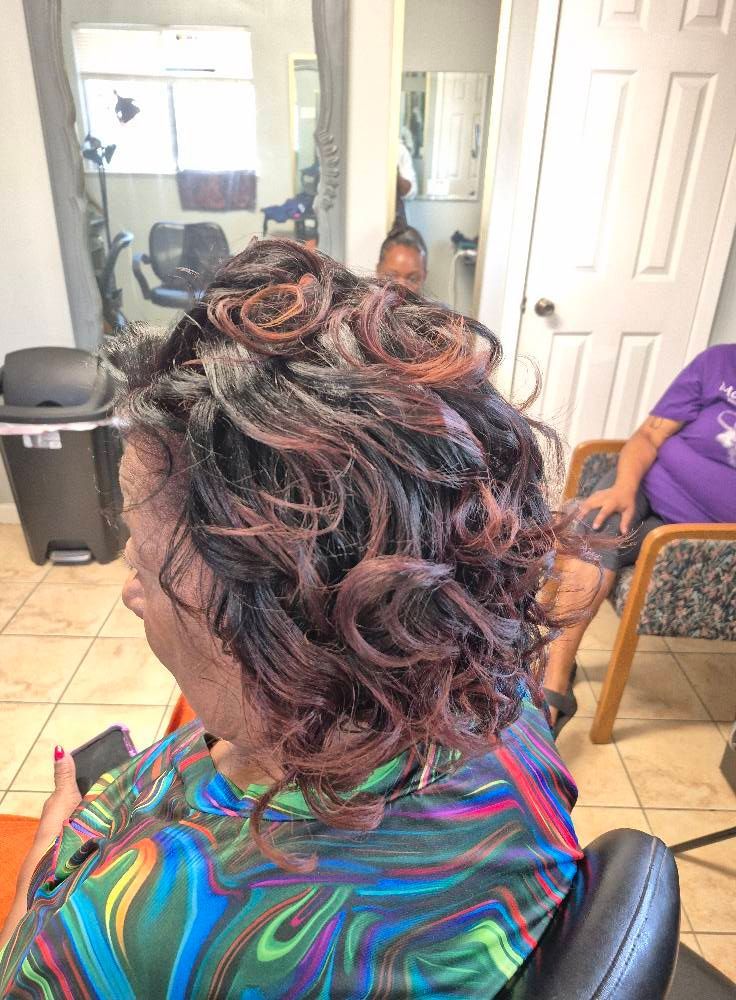 Woman with dark, curly hair with reddish highlights sits in a salon chair.