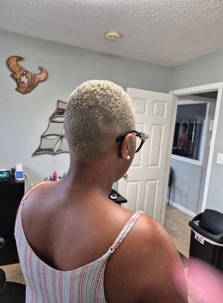 Woman with short, light-colored hair, wearing glasses and a camisole, facing away from the camera in a room.