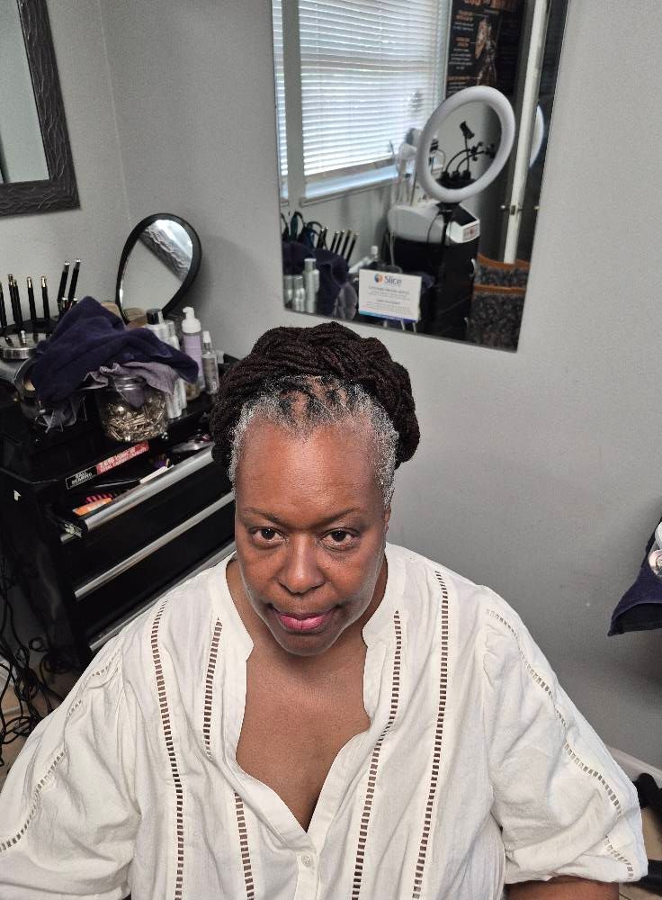 Person with dark hair and white shirt, in a room with a mirror and makeup supplies.