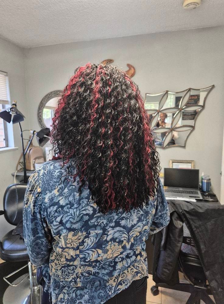 Woman with long, curly hair, partly red and black, in a room with a desk and decor.