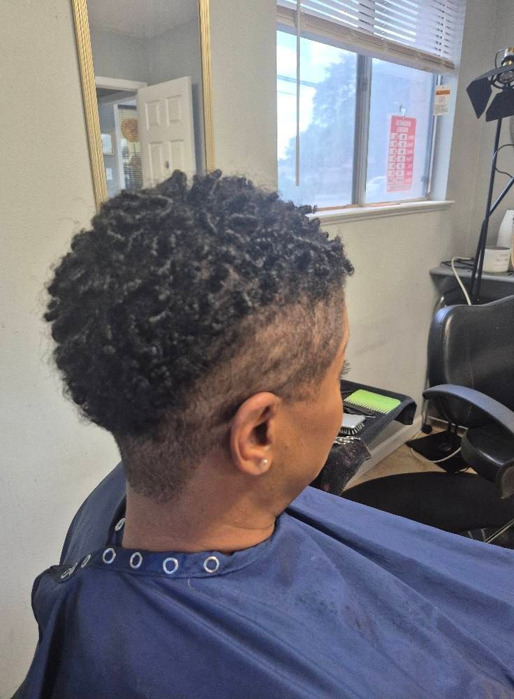 Person with short, textured hair and a shaved side; seated in a salon chair.