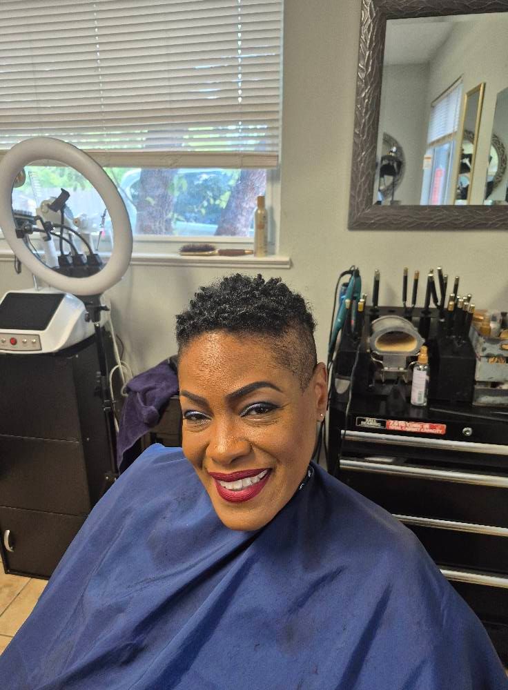 Woman with short, textured hair smiles in a salon, wearing a blue cape.