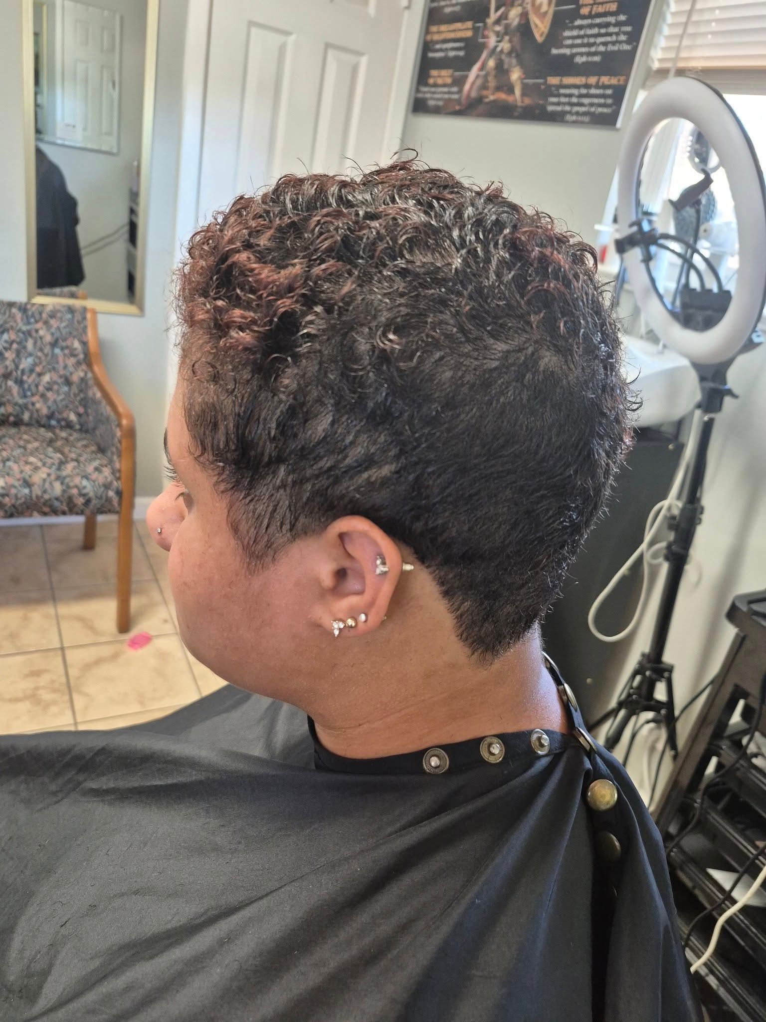 Person with a short, textured hairstyle in a salon, wearing a salon cape.