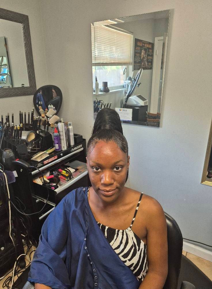 Woman with updo in salon, wearing animal print top and blue cape, looking at camera.