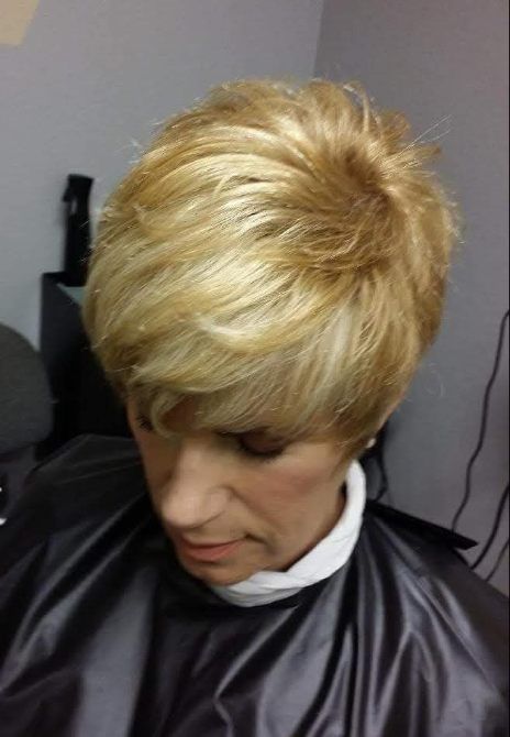 Woman with short, layered blonde hair in a salon setting, looking down.