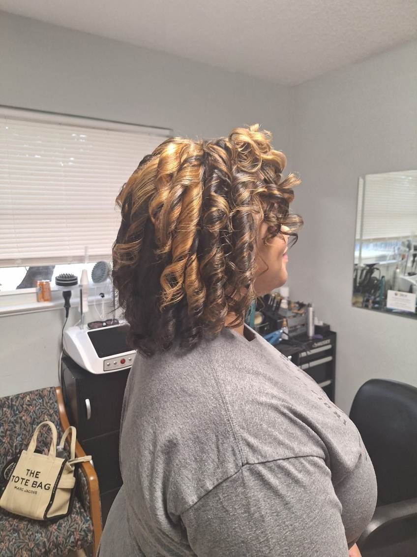 Woman with curly, layered hair; indoors near a window and mirror.