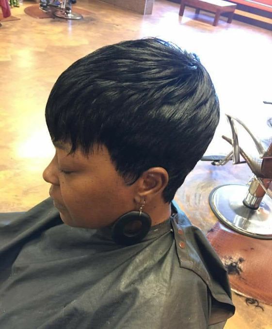 Woman with a black, short layered haircut, wearing black earrings, and a cape in a salon.