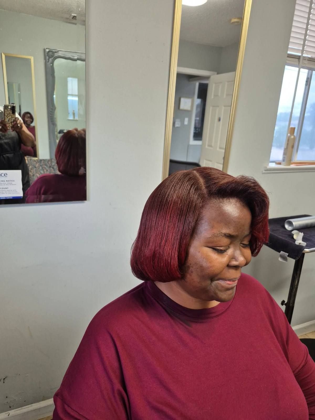 Woman with burgundy bob hairstyle, wearing a burgundy shirt, in a salon setting.