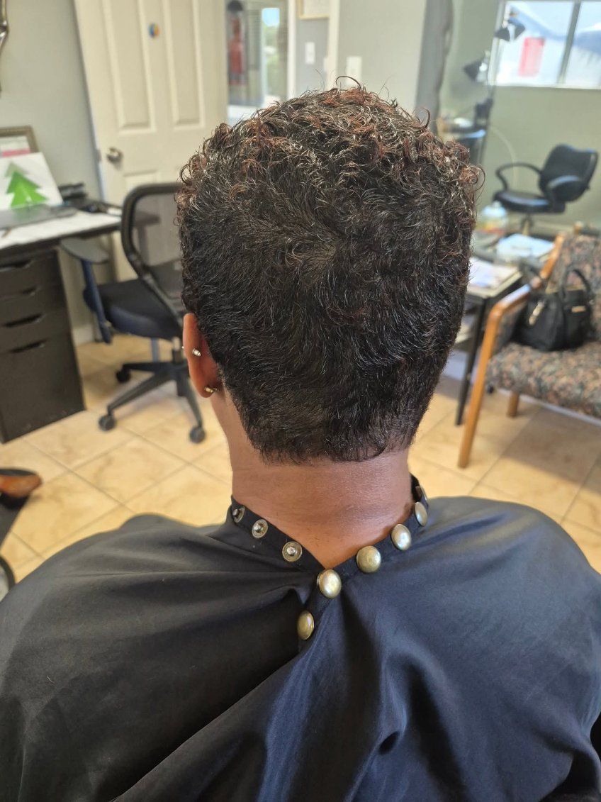 Back view of a person with short, textured dark hair, wearing a salon cape.