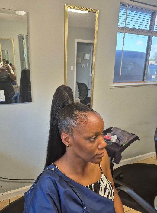 Woman with high ponytail, in salon setting, looking to the side. Wearing a blue cover-up and patterned top.