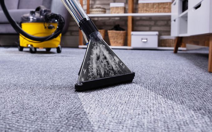 Carpet cleaner vacuuming a light gray rug in a living room, leaving a clean stripe.
