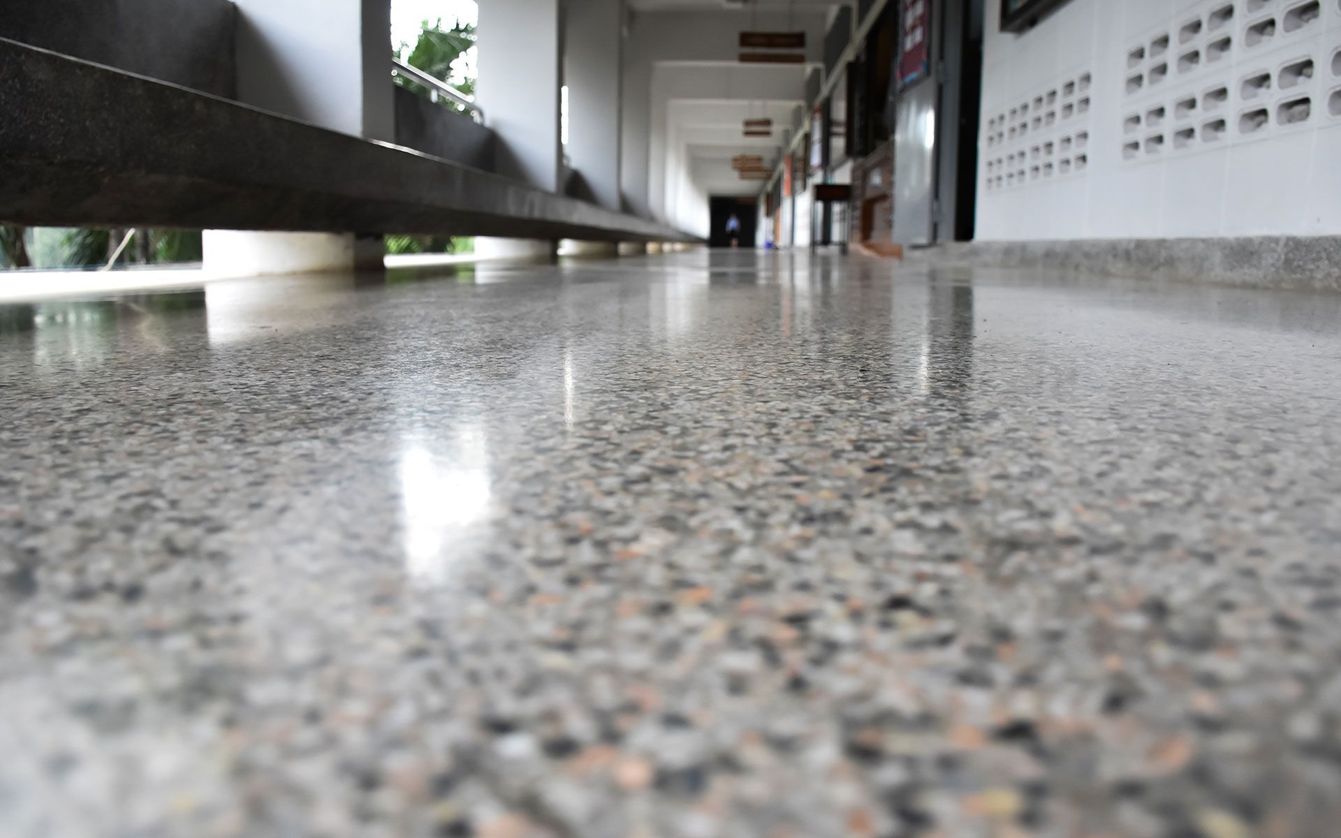 Close-up of polished concrete floor in a hallway, reflecting the environment with gray and tan speckled texture.