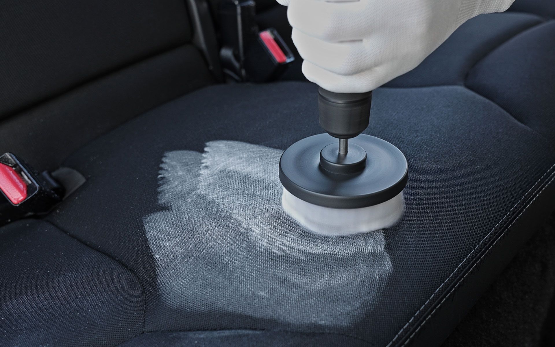 Person cleaning car seat with drill and brush.