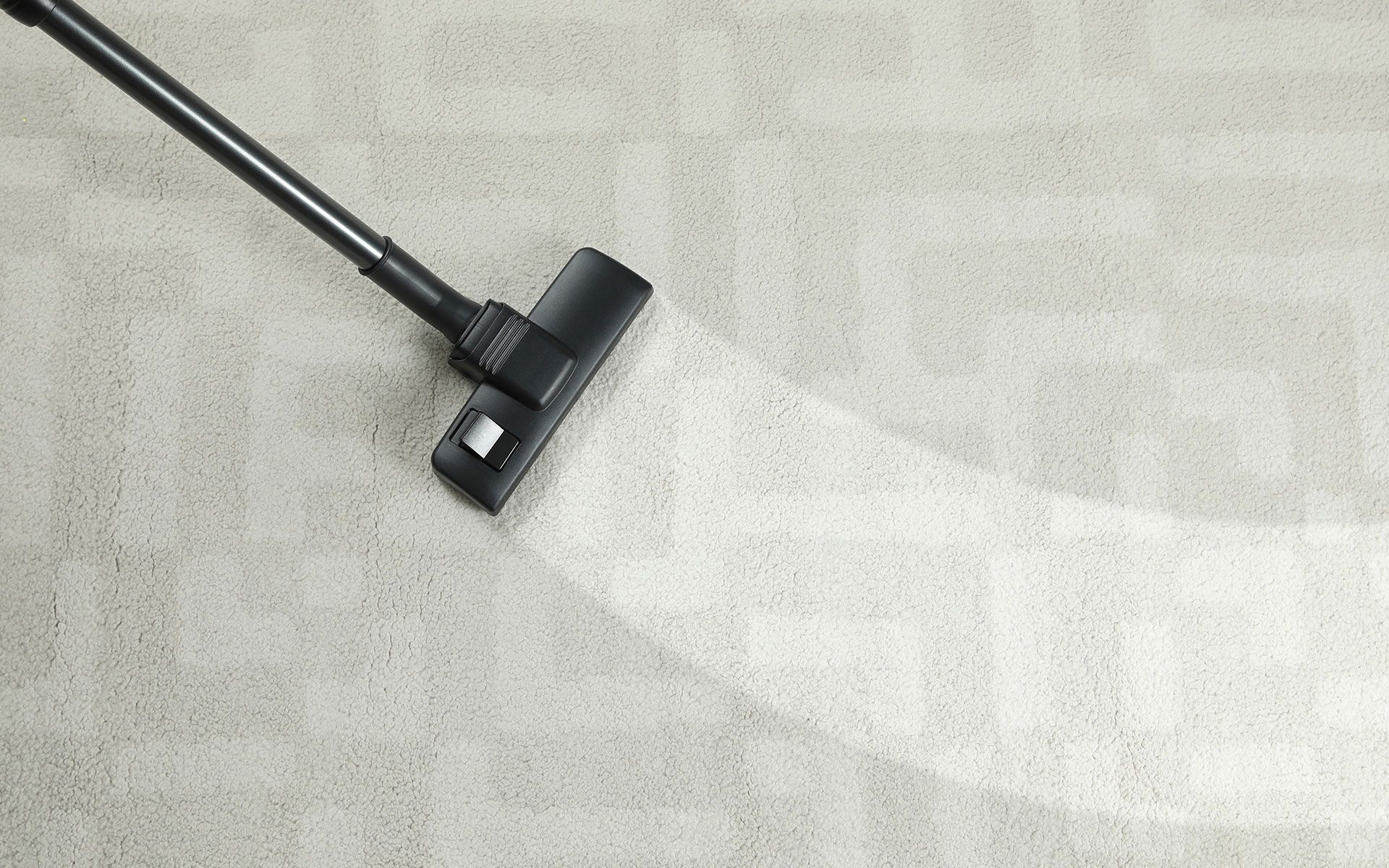 Vacuum cleaner cleaning a light-colored carpet, leaving a clean path behind it.