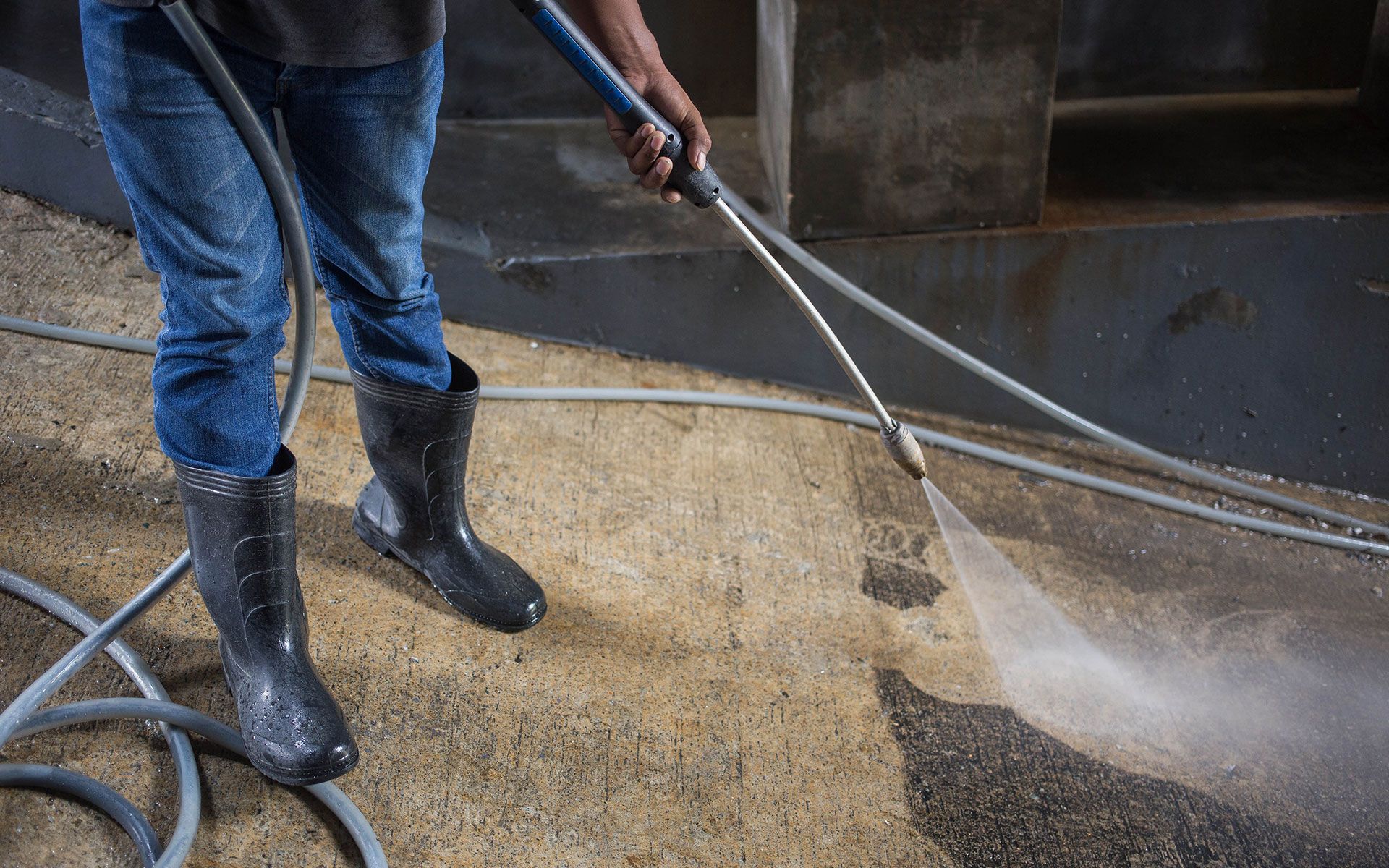 Person in boots power washing a concrete surface.