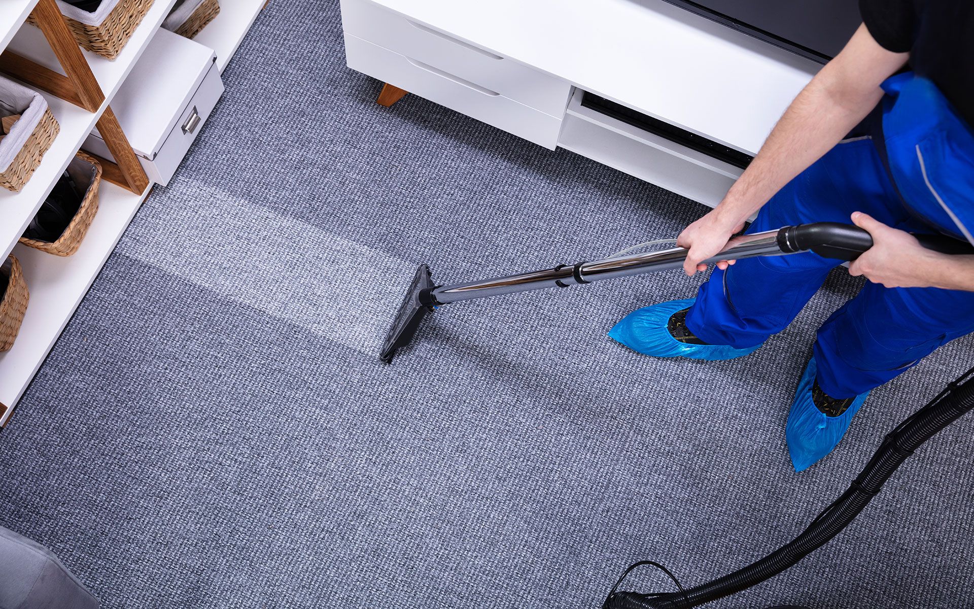 Person cleaning a gray carpet with a cleaning machine; visible cleaned and uncleaned sections.