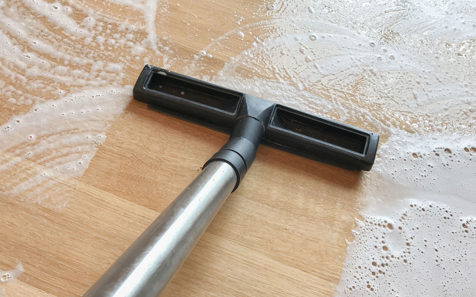 Floor being cleaned with a vacuum attachment, creating soapy water and leaving streaks.