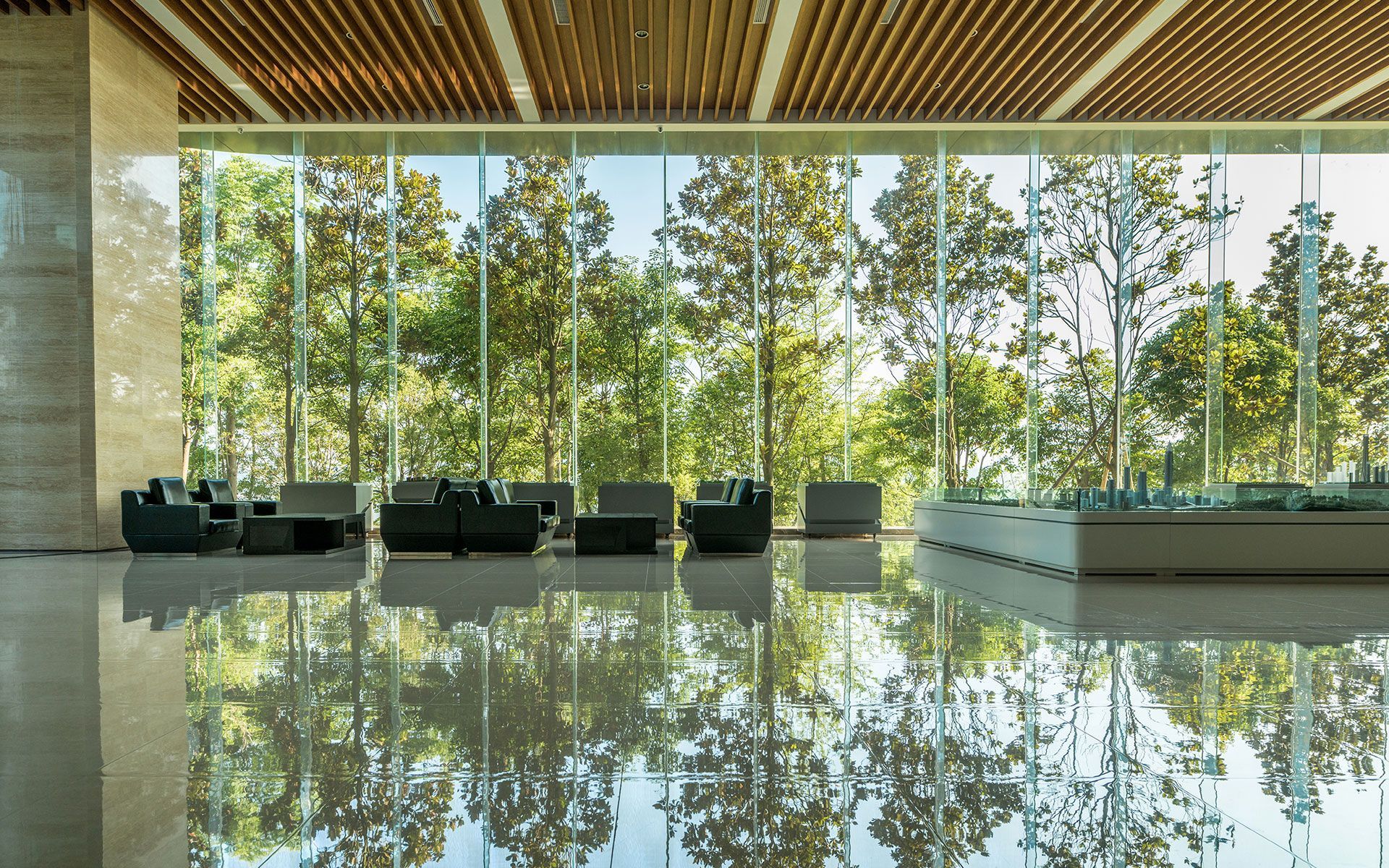 Interior lobby with mirrored floor, floor-to-ceiling windows, and seating overlooking a tree-filled landscape.