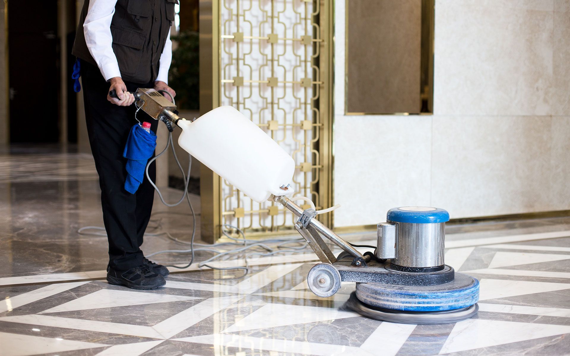 Person in uniform using a floor cleaning machine on a patterned, glossy floor.