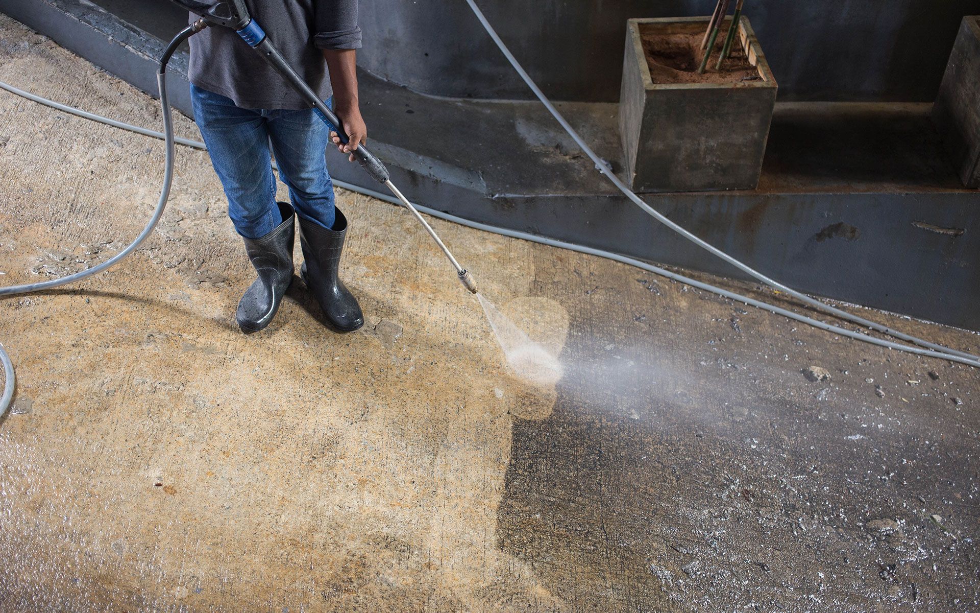 Person in boots pressure washing a concrete floor.