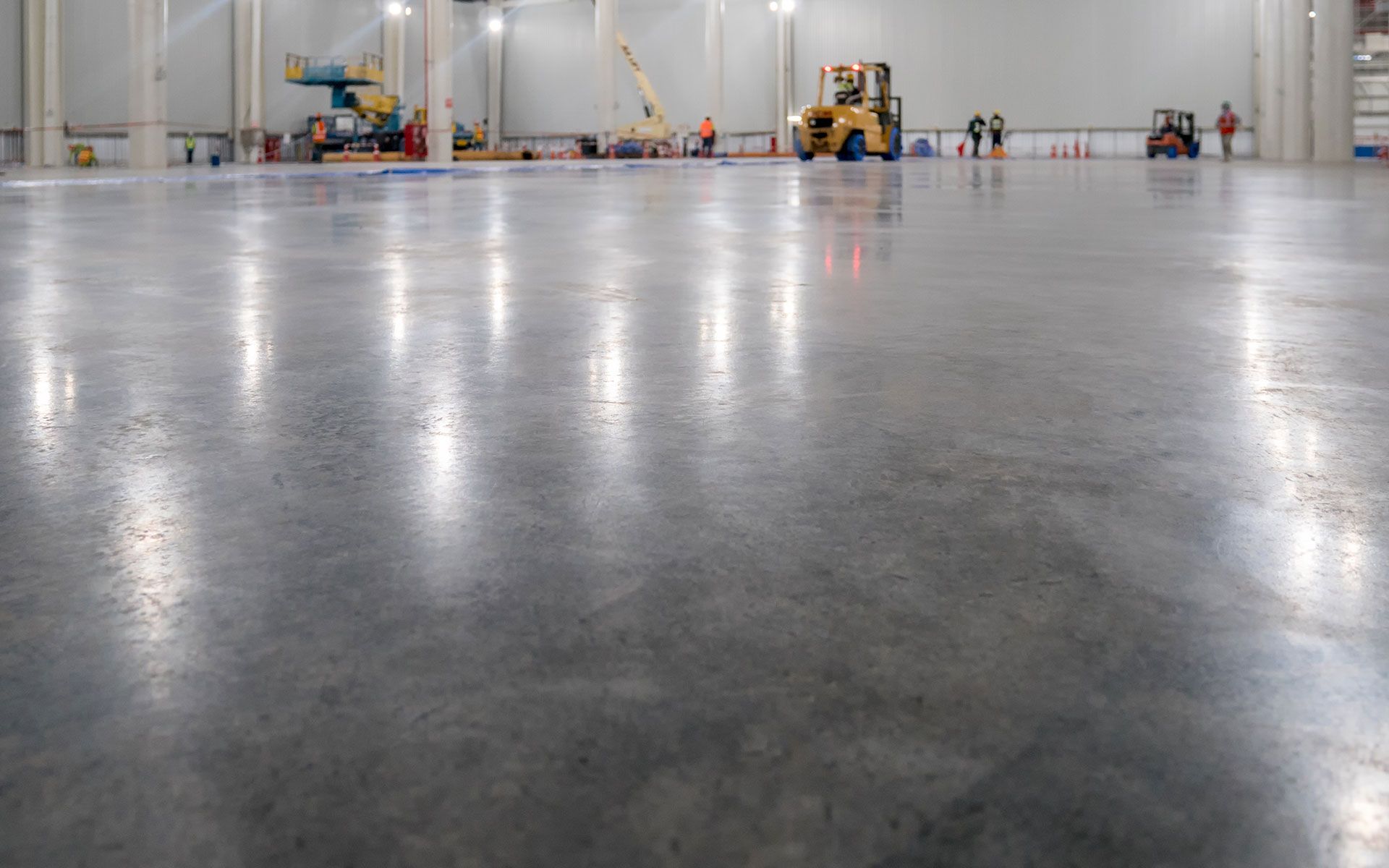 Polished concrete floor in a large industrial warehouse, reflecting overhead lights.
