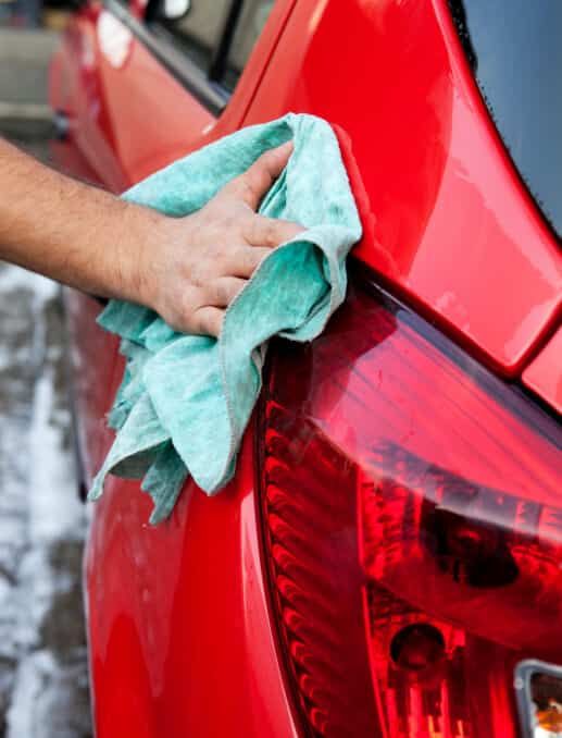 a person is cleaning a red car with a towel